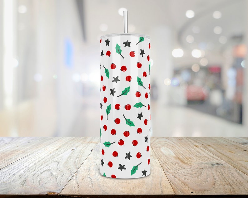 Puede incluir: Un vaso blanco con un patr&oacute;n de bayas de acebo rojas y verdes y estrellas.