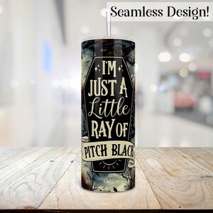 May include: A black and white tumbler with a spooky design. It features a coffin with the text "I'm just a little ray of pitch black".