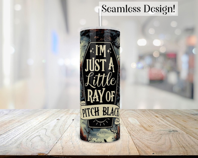 May include: A black and white tumbler with a spooky design. It features a coffin with the text "I'm just a little ray of pitch black".