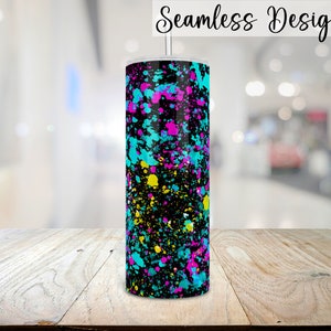 Puede incluir: Un vaso negro con un dise&ntilde;o de pintura salpicada de colores. Los colores son turquesa, amarillo, rosa y negro. El vaso est&aacute; sobre una superficie de madera.