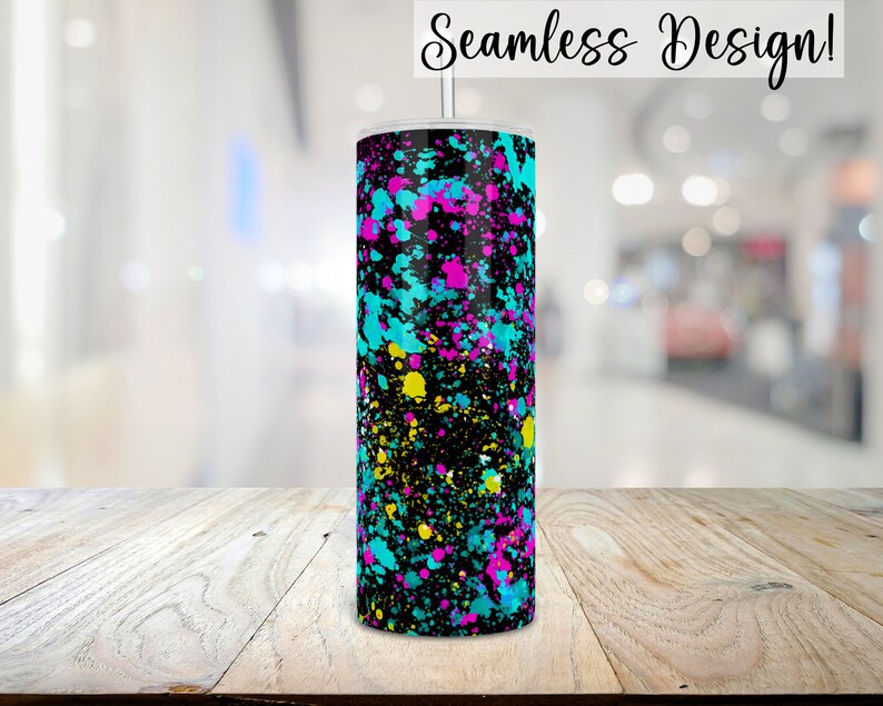 Puede incluir: Un vaso negro con un dise&ntilde;o de pintura salpicada de colores. Los colores son turquesa, amarillo, rosa y negro. El vaso est&aacute; sobre una superficie de madera.
