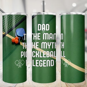 May include: A green and tan stainless steel tumbler with a white design that reads "Dad the man the myth the pickleball legend". The tumbler has a white pickleball paddle design on the bottom and a green pickleball net and orange pickleballs on the top.
