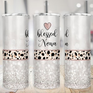 May include: Three stainless steel tumblers with a white background and a pink heart with the text "blessed Nona" on the center tumbler. The tumblers have a rose gold and leopard print design.