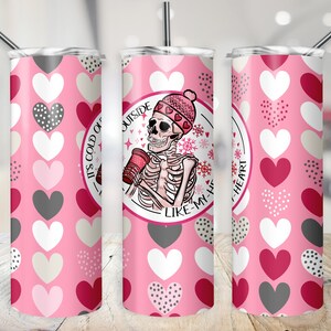 May include: A pink stainless steel tumbler with a white skeleton wearing a pink and white hat holding a cup of coffee. The tumbler has a white and gray heart pattern. The text on the tumbler reads "It's cold outside like my heart".