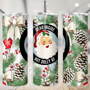May include: A white tumbler with a Christmas-themed design. The tumbler features a Santa Claus illustration with the text "Dead Inside But Jolly AF". The design also includes pine cones, holly berries, and bows.