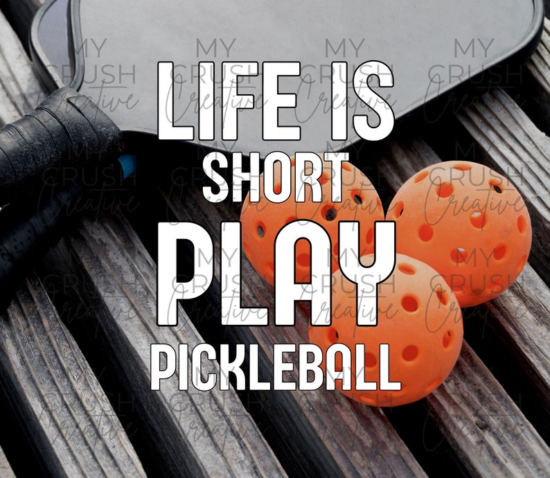 K&ouml;nnte beinhalten: Ein schwarzer Pickleball-Schl&auml;ger mit dem Text "Life is Short Play Pickleball" in wei&szlig;en Buchstaben. Drei orangefarbene Pickleball-B&auml;lle befinden sich im Vordergrund.