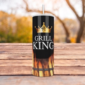 May include: A stainless steel tumbler with a black background and the words "GRILL KING" in white. A gold crown and grill tools graphic are above the text. The bottom of the tumbler features a flame design. A silver straw is inserted in the lid.