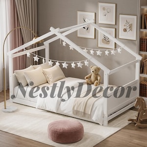May include: A white wooden house-shaped bed frame featuring a pitched roof design. The bed is dressed with white bedding, two beige pillows, and a beige throw blanket. A string of white star-shaped decorations hangs from the frame, and a teddy bear sits on the mattress.