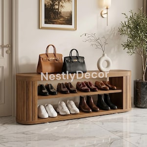May include: A wooden shoe rack with two shelves holding various footwear including dress shoes, boots, and sneakers. On top sit a tan leather handbag, a black leather handbag, and a white ceramic vase. The text NestlyDecor is visible.