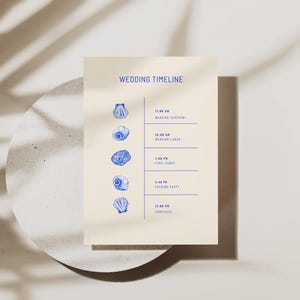 May include: A rectangular wedding timeline card on a cream background featuring blue text and illustrations of five different seashells. The text reads WEDDING TIMELINE, 11:00 AM WEDDING CEREMONY, 12:00 PM WEDDING LUNCH, 1:00 PM FIRST DANCE, 4:00 PM EVENING PARTY, 11:00 PM CARRIAGES.
