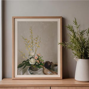 以下が含まれることがあります： 白いバラ、小さなピンクの花、背の高い黄色い花を活けた花瓶、小さな茶色のティーポットとカップが、ドレープのかかった布の上に置かれている様子を描いた額装アートプリント。