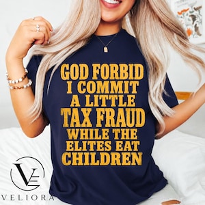 May include: A navy blue short-sleeved t-shirt featuring bold, distressed yellow text that reads: GOD FORBID I COMMIT A LITTLE TAX FRAUD WHILE THE ELITES EAT CHILDREN. The shirt has a crew neckline and a standard fit, displaying the printed graphic clearly.