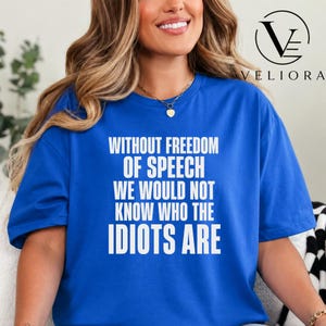 May include: A royal blue short-sleeved t-shirt featuring white text printed on the front that reads: WITHOUT FREEDOM OF SPEECH WE WOULD NOT KNOW WHO THE IDIOTS ARE. The shirt has a crew neckline and a relaxed fit, showcasing bold typography.