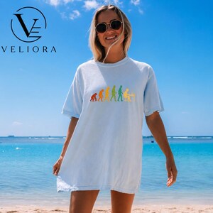 Pu&ograve; includere: Una t-shirt a maniche corte color azzurro con una stampa grafica colorata dell'evoluzione umana, che parte da un primate e termina con una persona seduta a una scrivania con computer. La maglietta ha un girocollo e una vestibilit&agrave; ampia.