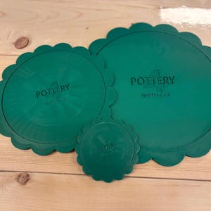 May include: Three circular, dark green silicone lids with scalloped edges. Each lid features the embossed text "4 POTTERY" and the website "4pottery.ca" in the centre. The lids are presented in three different sizes, ranging from small to large.