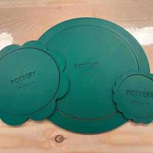 May include: Three dark green circular lids of varying sizes. The largest is a plain circle, while the two smaller ones feature scalloped edges. Each lid is embossed with the text 4POTTERY and 4pottery.ca in the center of the surface.