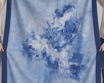 May include: A rectangular blanket featuring a central abstract pattern of swirling light blue, dark blue, and white colors. The blanket is framed by a solid dark blue border that runs along all four edges, creating a distinct contrast.