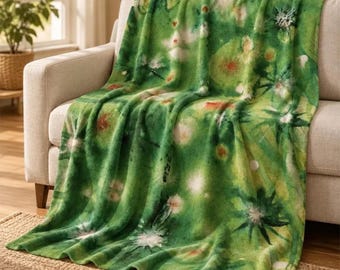 May include: A soft throw blanket featuring a vibrant green watercolor-style print with abstract white and dark green star-shaped floral patterns and soft, blurred circular accents throughout the fabric surface.