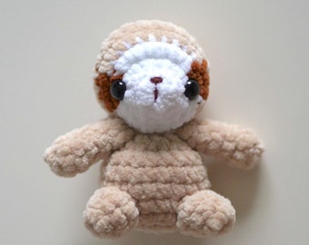 May include: A crocheted sloth toy with brown, white and beige fur. The sloth has black eyes and a small, pink nose.