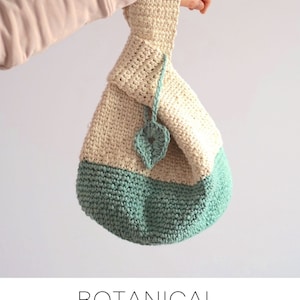 May include: A crocheted bag with a cream top and a teal bottom. The bag has a leaf design on the front and is tied with a cream cord. The bag is held by a hand wearing a light pink sweater. The text "BOTANICAL JAPANESE KNOT BAG" and "free crochet pattern @sweetsofties" is below the image.