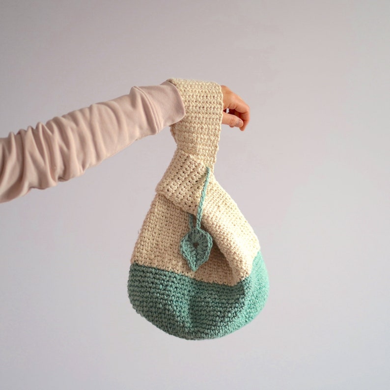 May include: A crocheted bag with a cream top and a light green bottom. The bag has a leaf-shaped detail on the front.