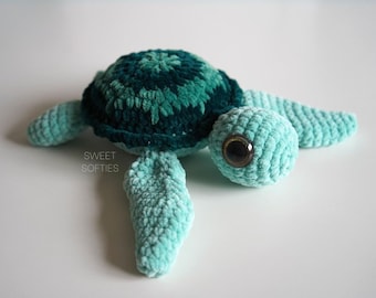May include: A crocheted sea turtle plush toy with a green shell and light blue body. The toy has large, black eyes and a sweet expression.