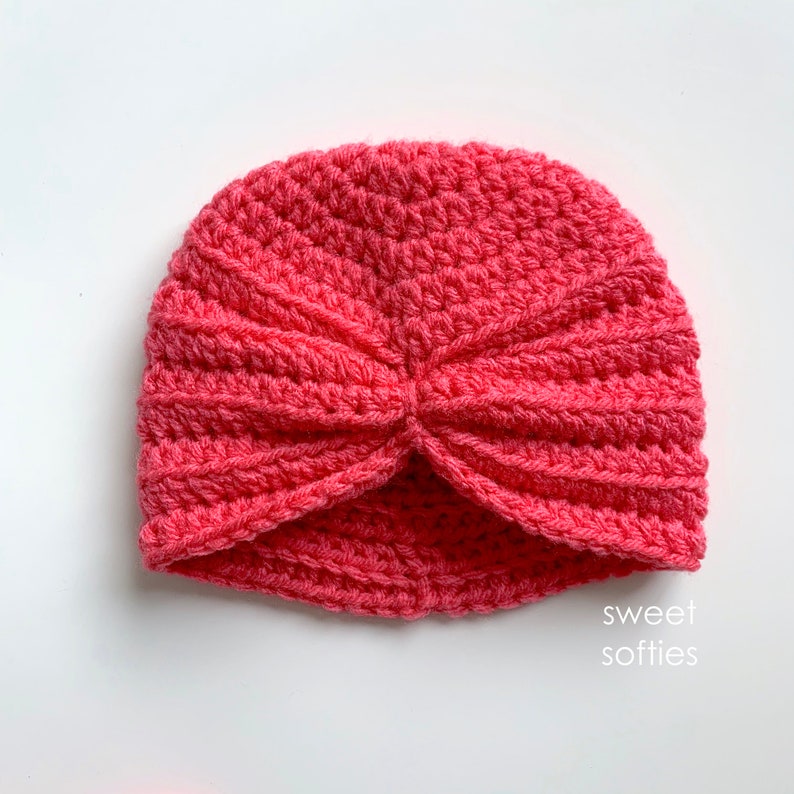 May include: A pink crocheted turban hat. The hat is folded in the front to create a turban style. The hat is made with a single crochet stitch.