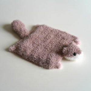 Peut inclure: Un jouet pour bébé fait à la main, en peluche rose et blanc, en forme de petit animal. Le jouet a une longue queue et une tête avec un museau blanc et un œil noir. Les mots "SWEET SOFTIES" sont imprimés au bas du jouet.