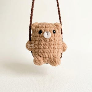 May include: A light brown crocheted bear bag with a dark brown strap. The bear features black plastic eyes, a white stitched muzzle, and the text SWEET SOFTIES printed on its side. The plush texture is consistent throughout the bear-shaped body.