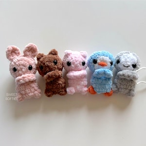 May include: Five crocheted stuffed animals in different colors and animal shapes. The animals are a pink bunny, a brown bear, a pink pig, a blue penguin, and a gray sloth.