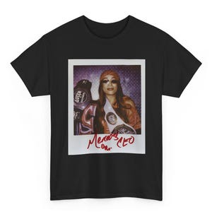 May include: A black short-sleeve t-shirt featuring a rectangular graphic print of a Polaroid-style photograph. The image shows a person wearing a headscarf, sunglasses, and a championship belt, with the red handwritten text "Mercedes CEO" below.