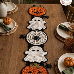 Könnte beinhalten: Ein gehäkelter Tischläufer zum Thema Halloween mit einer vertikalen Abfolge von zwei orangefarbenen Kürbissen, zwei weißen Gespenstern und einem zentralen weißen Spinnennetzmotiv, ergänzt durch kleine schwarze Häkelspinnen an den Seiten.