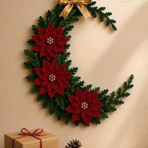 Puede incluir: Un adorno de pared en forma de media luna hecho de follaje verde tejido a ganchillo y tres flores de pascua rojas tejidas a ganchillo con cuentas doradas en el centro. Un lazo dorado corona la pieza y el logo BloomRunner Crochet es visible.