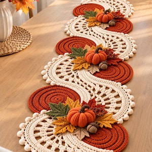 May include: A long, serpentine crochet table runner featuring alternating cream-colored lace sections and solid burnt orange circular mats. The runner is decorated with three-dimensional crocheted orange pumpkins, brown acorns, and multi-colored maple leaves.