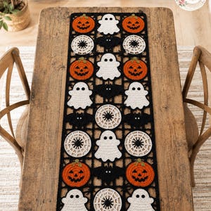 May include: A rectangular crochet table runner featuring a repeating pattern of orange jack-o'-lanterns, white ghosts, black bats, and white spider webs, all connected by a black grid border. The design elements are arranged in a grid layout.