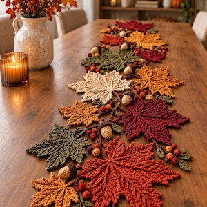 May include: A crochet table runner featuring a collection of interconnected maple leaves in shades of red, orange, yellow, and green, accented with small crocheted acorns and clusters of berries, creating a textured autumn-themed centerpiece.