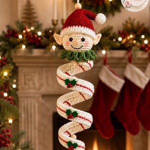 May include: A crocheted elf ornament featuring a red and white hat, a green collar, and a long, spiraling white body accented with thin red stripes and small green holly leaf and red berry embellishments, ending in a white pom-pom.