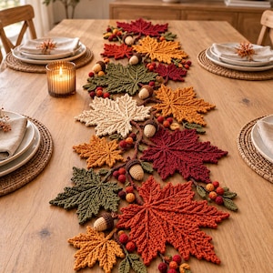 May include: A crochet table runner featuring a collection of autumn-themed maple leaves in shades of red, orange, yellow, and green, accented with small crocheted acorns and clusters of red berries arranged in a decorative, elongated vine pattern.