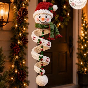 Könnte beinhalten: Ein hängendes Häkel-Schneemann-Ornament mit roter Mütze, grünem Schal und einem weißen, spiralförmigen Körper, der mit kleinen Pfefferminzbonbons und Stechpalmenblättern verziert ist. Die Figur hängt an einer Schnur mit Holz- und grünen Perlen.