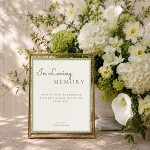 May include: A rectangular gold-toned metal frame holds a white sign with a scalloped green border. The text reads: In Loving MEMORY, HELD IN LOVE, REMEMBERED WITH JOY, MISSED TODAY AND EVERY DAY, 06.26.2027, ISABEL & JASON. The sign is displayed upright.