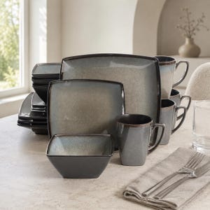 May include: A dinnerware set featuring square plates, bowls, and mugs with a reactive glaze finish in shades of blue and gray. The pieces have dark brown rims and a speckled texture, arranged in a stack with individual items placed in the foreground.