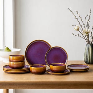 May include: A dinnerware set featuring plates and bowls with a gradient finish transitioning from deep purple in the center to a warm amber-brown at the edges. The collection includes various sizes of round plates and matching bowls with smooth surfaces.