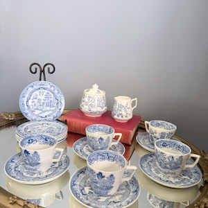 May include: A white porcelain tea set featuring a blue willow pattern. The set includes several teacups with matching saucers, a lidded sugar bowl, a small creamer jug, and a stack of small plates, all decorated with intricate blue landscape scenes.