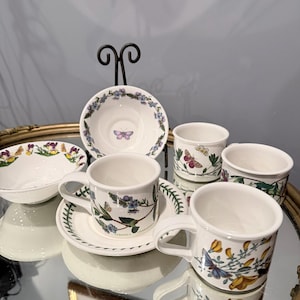 Peut inclure: Un ensemble de tasses et soucoupes en céramique blanche ornées d'illustrations botaniques colorées de fleurs et de papillons. Les pièces présentent des motifs floraux détaillés et diverses espèces de papillons, avec le texte Veronica Chamaedrys.