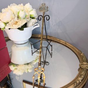 Peut inclure: Un long outil métallique de couleur laiton, doté d'un embout décoratif en forme de couronne au sommet et d'une base symétrique ornée à plusieurs dents. La tige métallique présente une texture torsadée et l'objet est posé sur un support.
