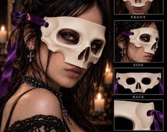 May include: A cream-colored skull mask featuring eye and nose cutouts, secured with purple satin ribbons. The mask is displayed in multiple views including front, side, back, and a close-up detail. The text ShadowGoth RELICS is visible.