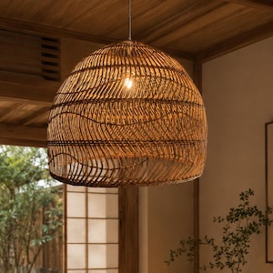 Peut inclure: Une grande suspension en forme de dôme fabriquée en rotin tressé marron. Le luminaire présente un motif complexe et superposé de brins d'osier horizontaux et incurvés, suspendu au plafond par un cordon fin, diffusant une lueur chaude.