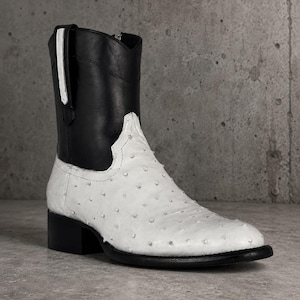 Könnte beinhalten: Ein zweifarbiger Stiefeletten-Stiefel mit einem glatten schwarzen Lederschaft und einem strukturierten weißen Ledervorderblatt mit markanter Punkttextur. Der Stiefel verfügt über einen schwarzen Blockabsatz, eine schwarze Sohle und eine weiße Zuglasche.