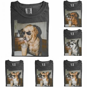 May include: A charcoal gray t-shirt featuring a graphic print of a dog wearing black sunglasses and drinking from a clear plastic cup with a straw. The shirt has a Comfort Colors brand label on the inside of the collar and is shown in six variations.