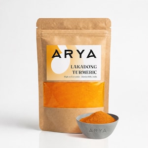 Peut inclure: Un sachet en papier brun contenant de la poudre de curcuma orange vif avec une étiquette indiquant ARYA LAKADONG TURMERIC High in Curcumin Jaintia Hills, India. Un petit bol gris rempli de la même poudre de curcuma est placé devant.